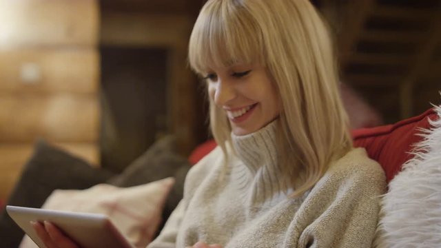Smiling young woman with tablet computer sitting on a couch in the living room. Shot on Red Epic.