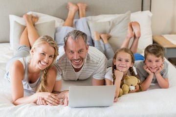Parents with their kids lying on bed and using laptop in bedroom