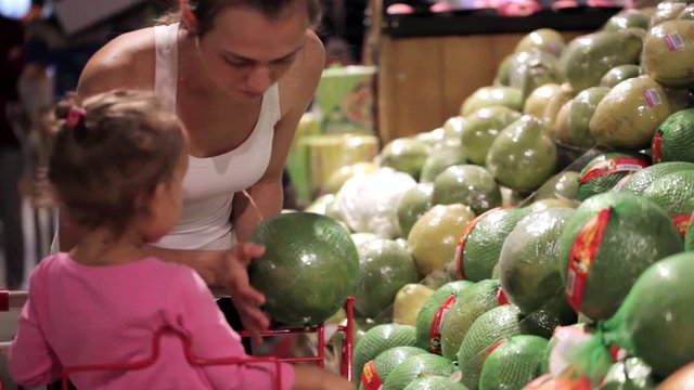 Young family of mother and little daughter choosing pomelo in supermarket.