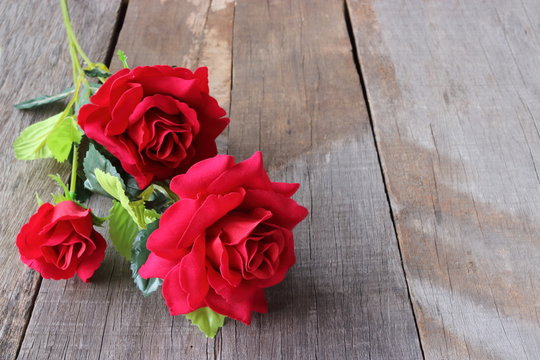 A beautiful bouquet of artificial red roses on old wooden board background with copy space. Valentine's day concept