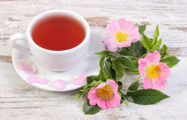 Cup of tea and wild rose flower on old rustic wooden background