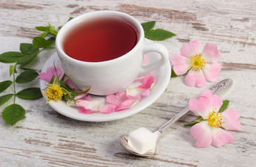 Fototapeta na wymiar Cup of tea and wild rose flower on old rustic wooden background