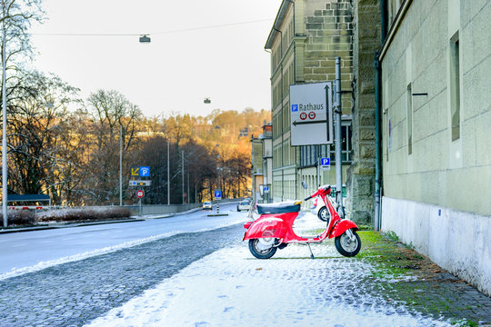 Red retro motorcycle scooter parked along a street covered with snow in the winter in the city of Bern, Switzerland.