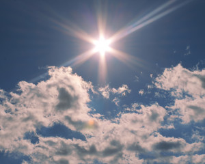 A blue sky with a sun flared and white clouds surrounding it.