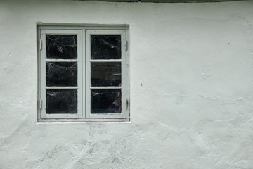One gray wood colonial style window, with spider web on the inside, fastened in a white painted plastered facade