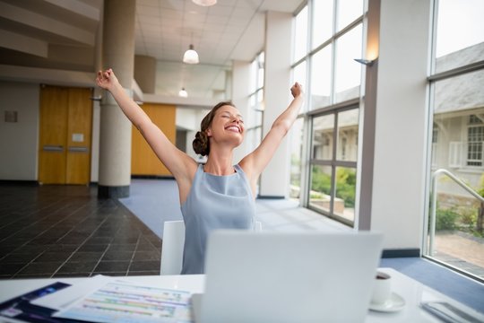 Businesswoman sitting at desk with arms outstretched