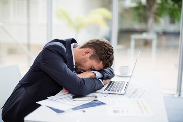 Tired businessman resting head on laptop at desk