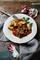 Beef bourguignon in ceramic plate with baked potatoes on metallic background. Rustic concept, natural light.