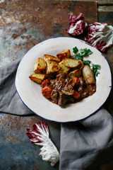Beef bourguignon in ceramic plate with baked potatoes on metallic background. Rustic concept, natural light.