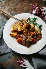 Beef bourguignon in ceramic plate with baked potatoes on metallic background. Rustic concept, natural light.