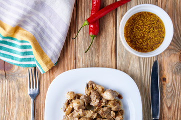 Beautifully served table in a rustic style. Plate with meat ragout of pork, beef, lamb and spices on the table. Plate with food, kitchen towel, hot chili peppers, bowl with French mustard. 
