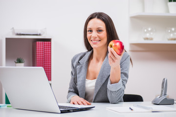Young businesswoman is eating apple in her office.