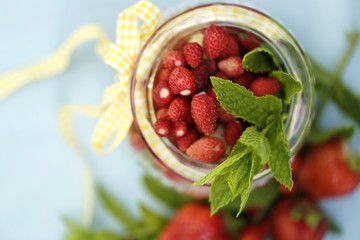 strawberry harvest. strawberries in a glass jar with a yellow ribbon and mint on blue cotton tablecloth 