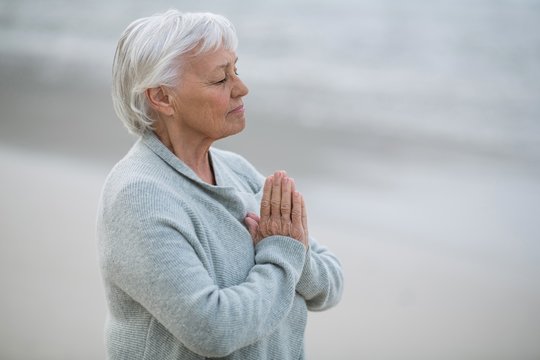 Senior woman praying on the beach - Powered by Adobe