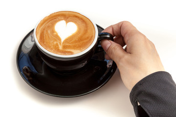 Coffee cup with heart shape latte art on top, hand holding the c