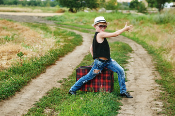 stylishly dressed boy in field with suitcase