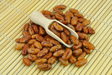 Brown pinto beans with wooden scoop on bamboo mat