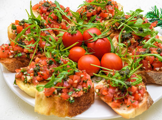 Tasty savory tomato Italian appetizers, or bruschetta, on slices of toasted baguette garnished with pesto and ruccola