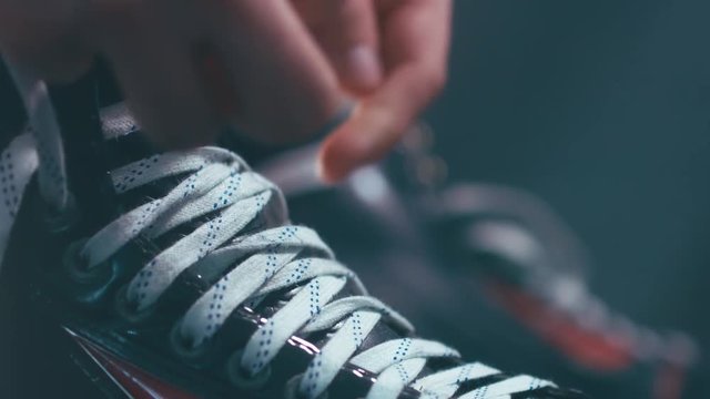 EXTREME CU Caucasian ice hockey player tightening laces on his skates in the locker room, preparing for the game. 4K UHD 60 FPS RAW edited footage