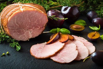 Smoked ham with herbs, fruits on black background