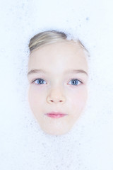 Little child blond girl in a bubble bath filled with soap foam