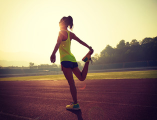 young fitness woman runner stretching legs on stadium track