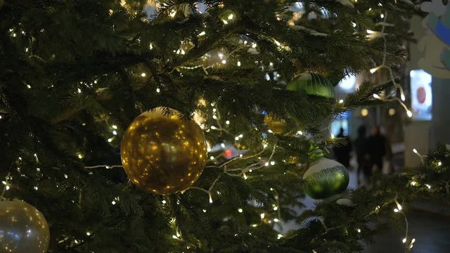 Christmas decoration balls hanging on tree on the background lights garland. Shiny yellow ball.