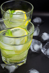 water with cucumber and lemon and ice on a black background