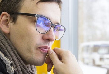 Young man in glasses and scarf looks thoughtfully out window