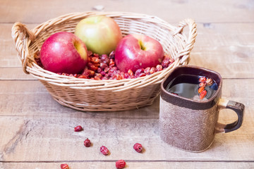 Tea and basket with dried wild roses and apples on wooden surfac