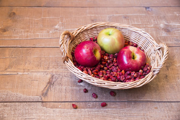 Basket with rosehip and red apples on wooden surface