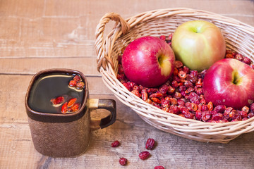 Rosehip and apple in basket next to cup of tea on wooden boards