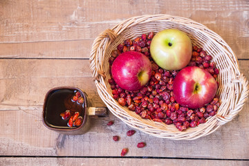 Basket with dried rosehip and apple and cup of tea rosehip on wo