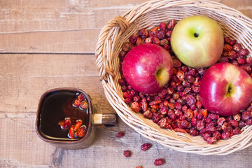 Mug of tea rosehip next to a wicker basket with apples and roseh