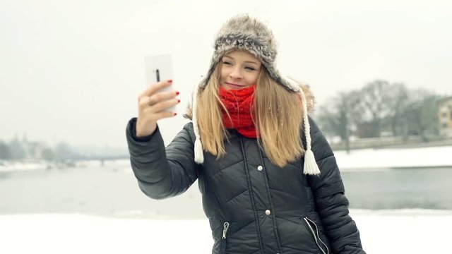 Happy girl doing selfies on smartphone while standing by the frozen river

