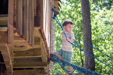 Little climber takes the rope bridge. Boy has fun time, kid climbing on sunny warm summer day