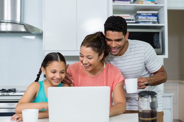 Parents and daughter using laptop in kitchen at home