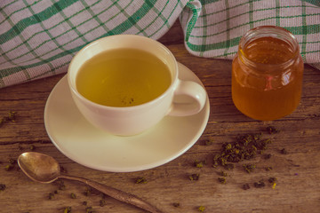 Green tea in a white cup and jar of honey with spoon and green k
