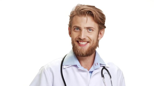 Confident Caucasian male doctor with light beard wearing medical overall showing ok with thumb on white background in slowmotion
