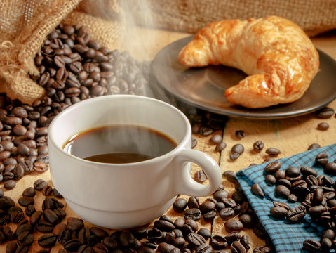 Hot coffee cup and baked croissants on wooden background