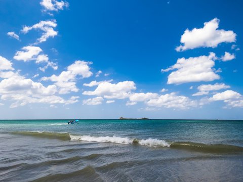 View of Pigeon Island Trincomalee from Beautiful White Sand turquoise water waves Beach with Blue Sky with White clouds and a boat in the back ground taking people to the island in Trincomalee