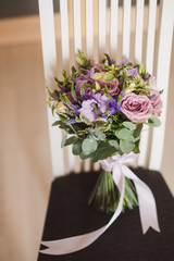 Bridal accessory. Beautiful bouquet of purple and pink flowers with eucalyptus on a chair.
