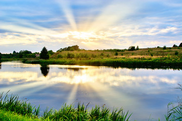 Summer landscape of sunset by the river with reflections