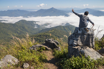 Obraz premium man sitting on the cliff and looking at the valley and mountains in the daylight
