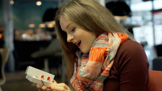 Girl looks happy while holding boc with present inside it and opens it
