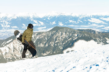 Fototapeta na wymiar Young snowboarder holding his board in hand and climbing to the top of a mountain