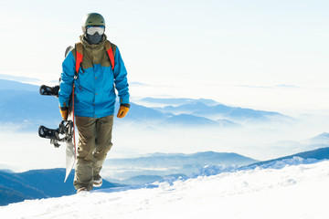 Young snowboarder walking up the mountain with snowboard in hand