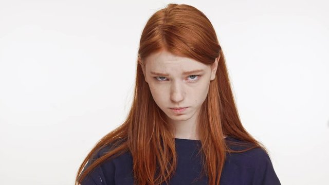 Cute upset Caucasian foxy teenage girl in dark blue t-shirt looking at camera begging on white background