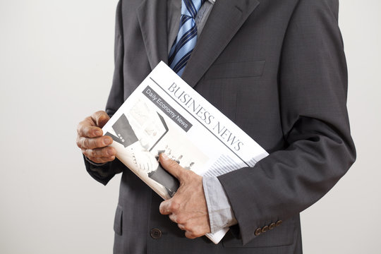 Businessman holding newspaper on gray background