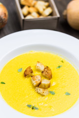Butternut Squash Soup Detail with Fried Bread Pieces on White Plate and Raw Ingredients on Background